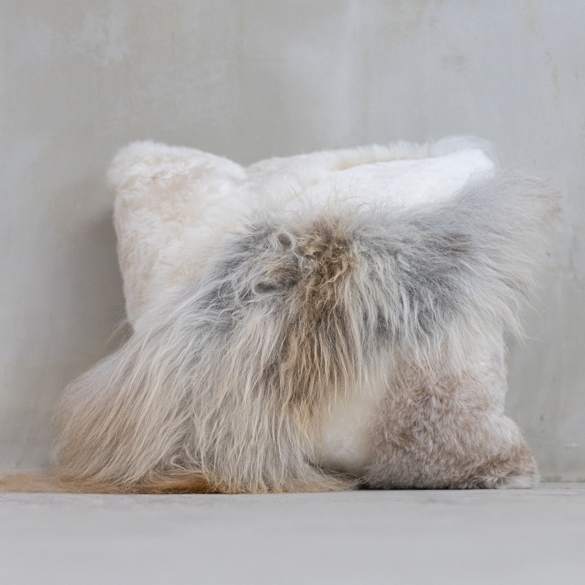 Coussin patchwork en peau de mouton multicolore posé au sol avec un coussin blanc