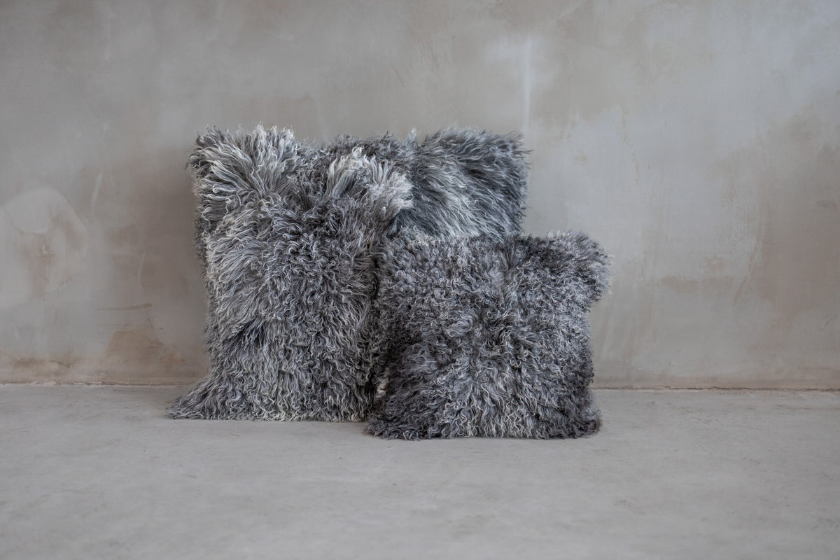 Coussins en peau de mouton du Tibet gris naturel posés contre un mur