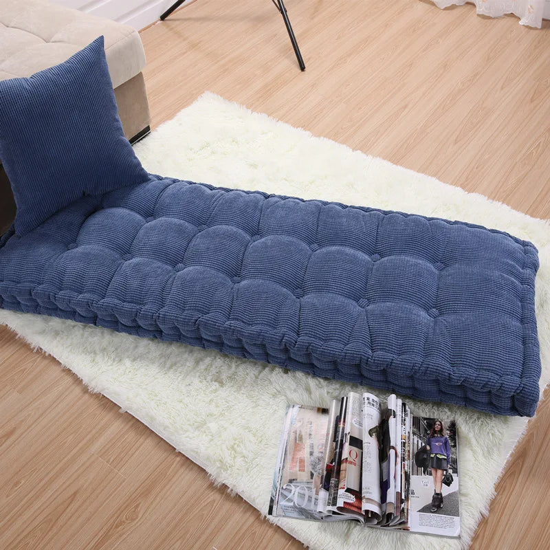 Coussin extérieur épais et rectangulaire ici de couleur bleu posé sur un tapis blanc.