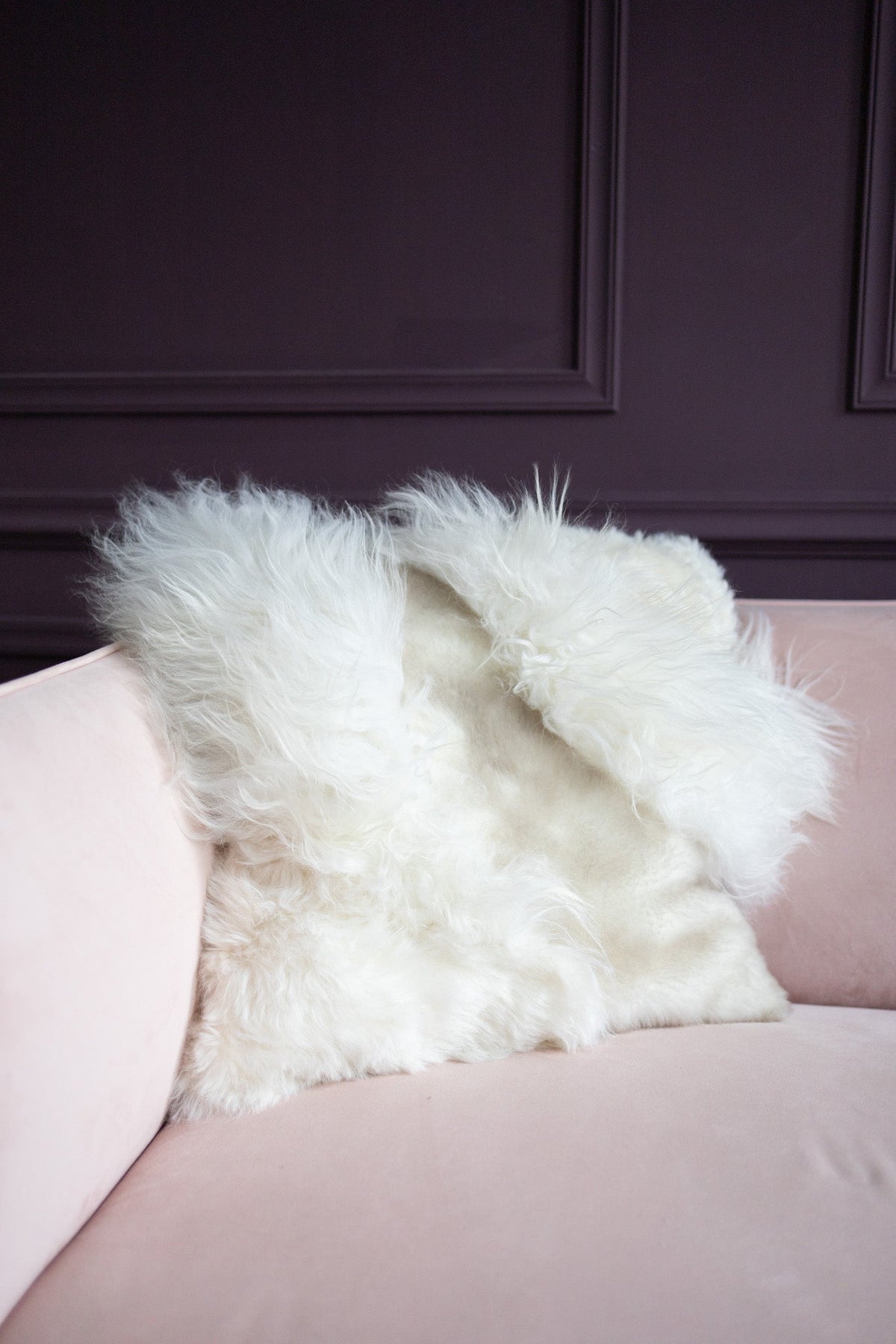 Housse garnie patchwork en peau de mouton blanc posée sur un canapé rose poudré